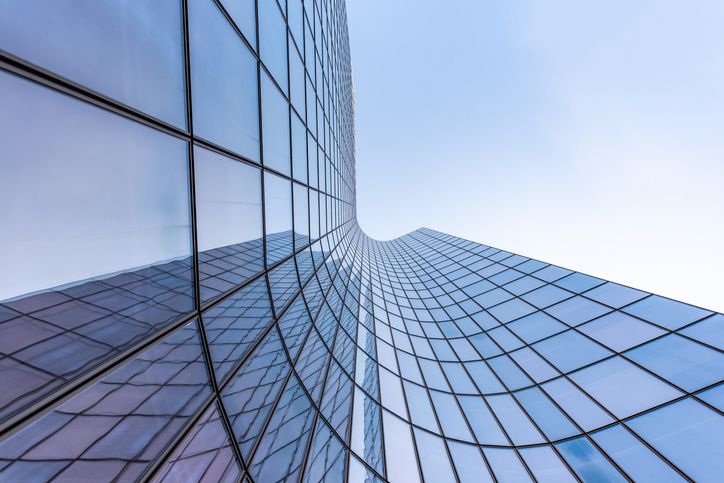 Wand eines architektonischen Glasebäudes in blau-lila Farbe dessen Konstruktion in einer Kurve von links nach rechts abfällt