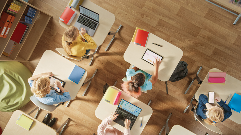 Ein Klassenzimmer mit mehreren Schülern die an Einzeltischen mit Tablets und Laptops sitzen von oben fotografiert